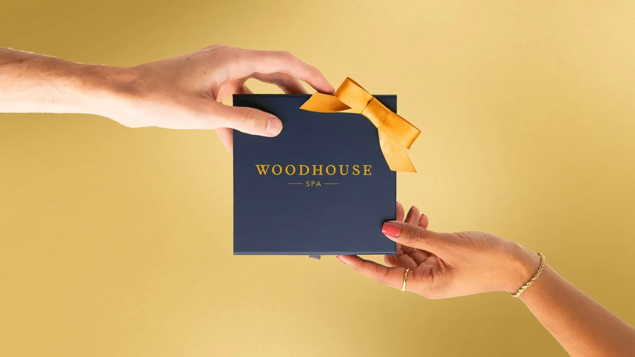Photo of two hands holding Woodhouse Spa gift box against gold background