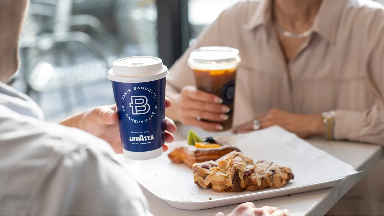 Photo of two people sitting at table with pastries, holding Paris Baguette coffee beverages