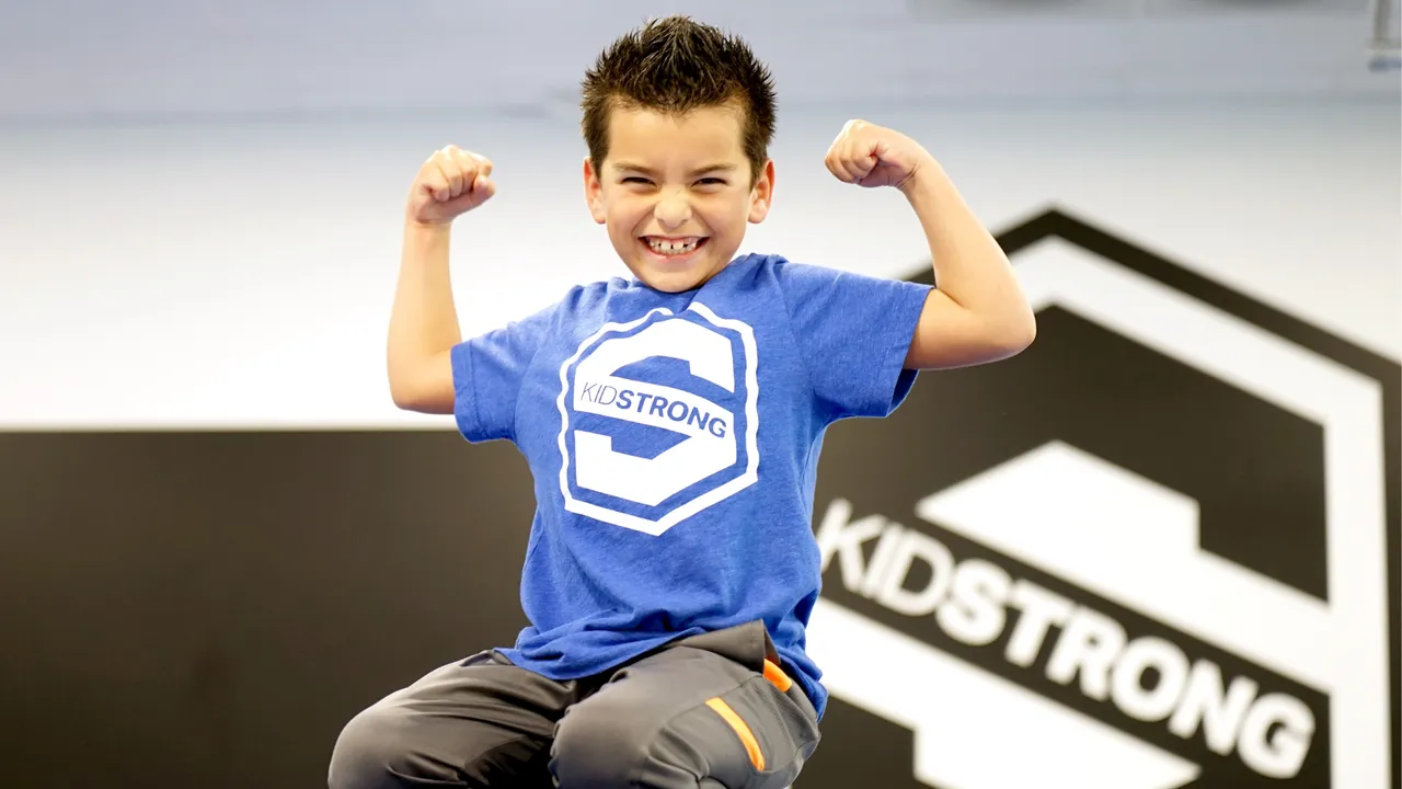 Photo of young child wearing blue KidStrong shirt, sitting on knees