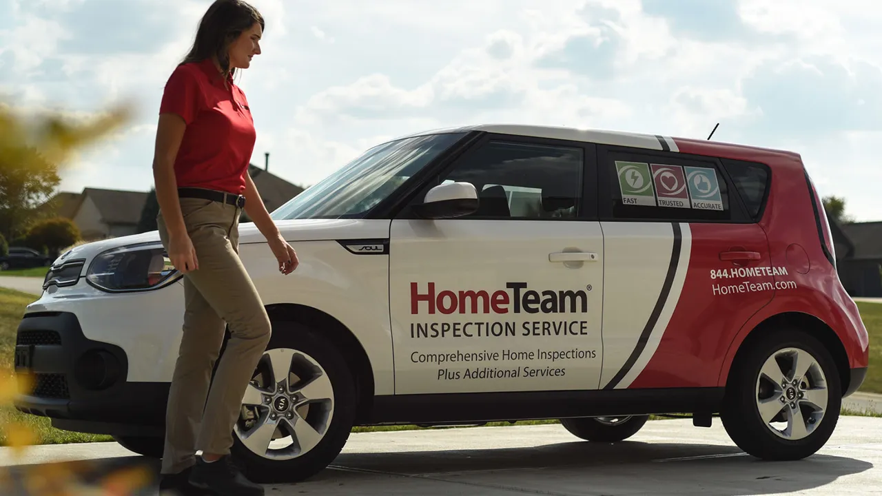 Photo of HomeTeam inspector in red polo and khaki pants, walking by branded vehicle