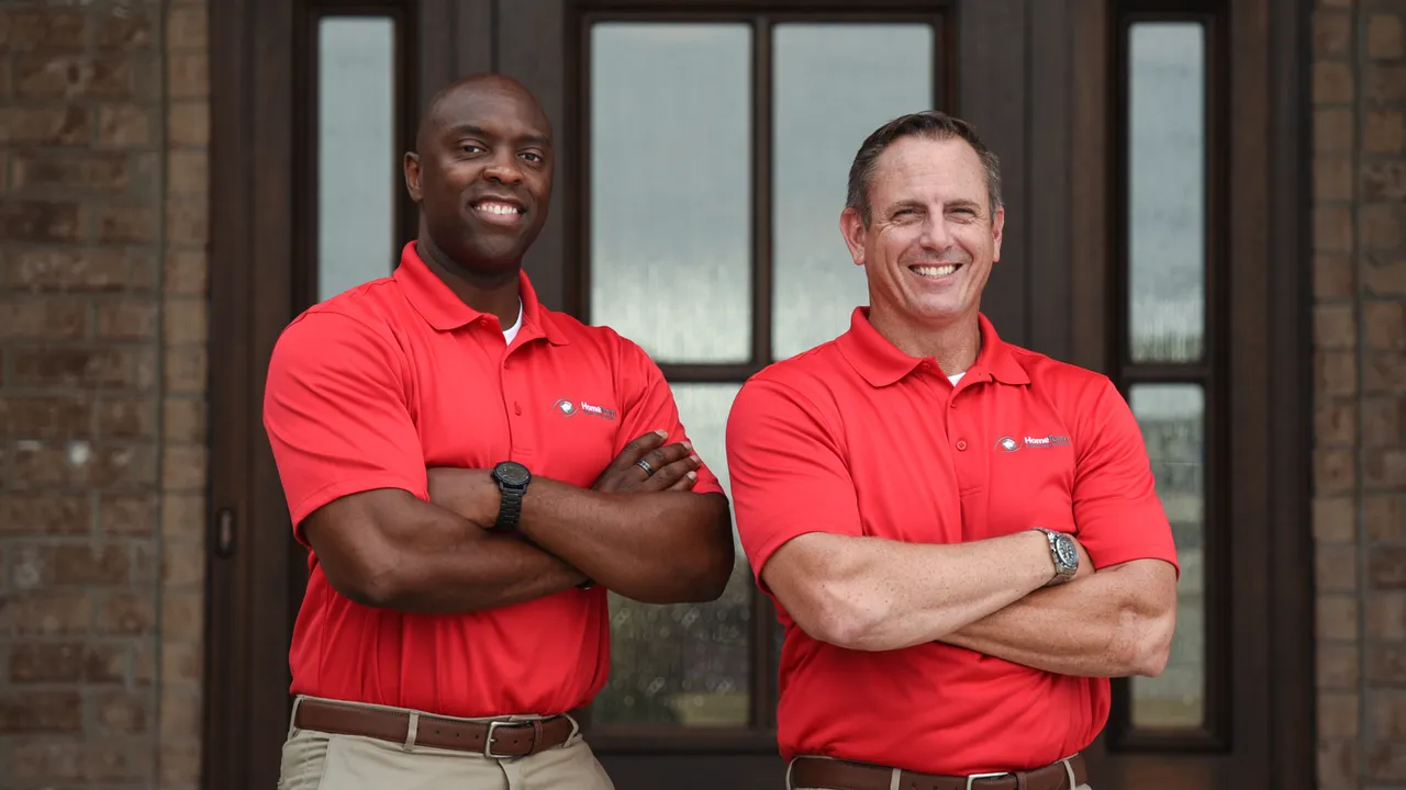 Photo of two HomeTeam team members standing in front of home, arms crossed, smiling
