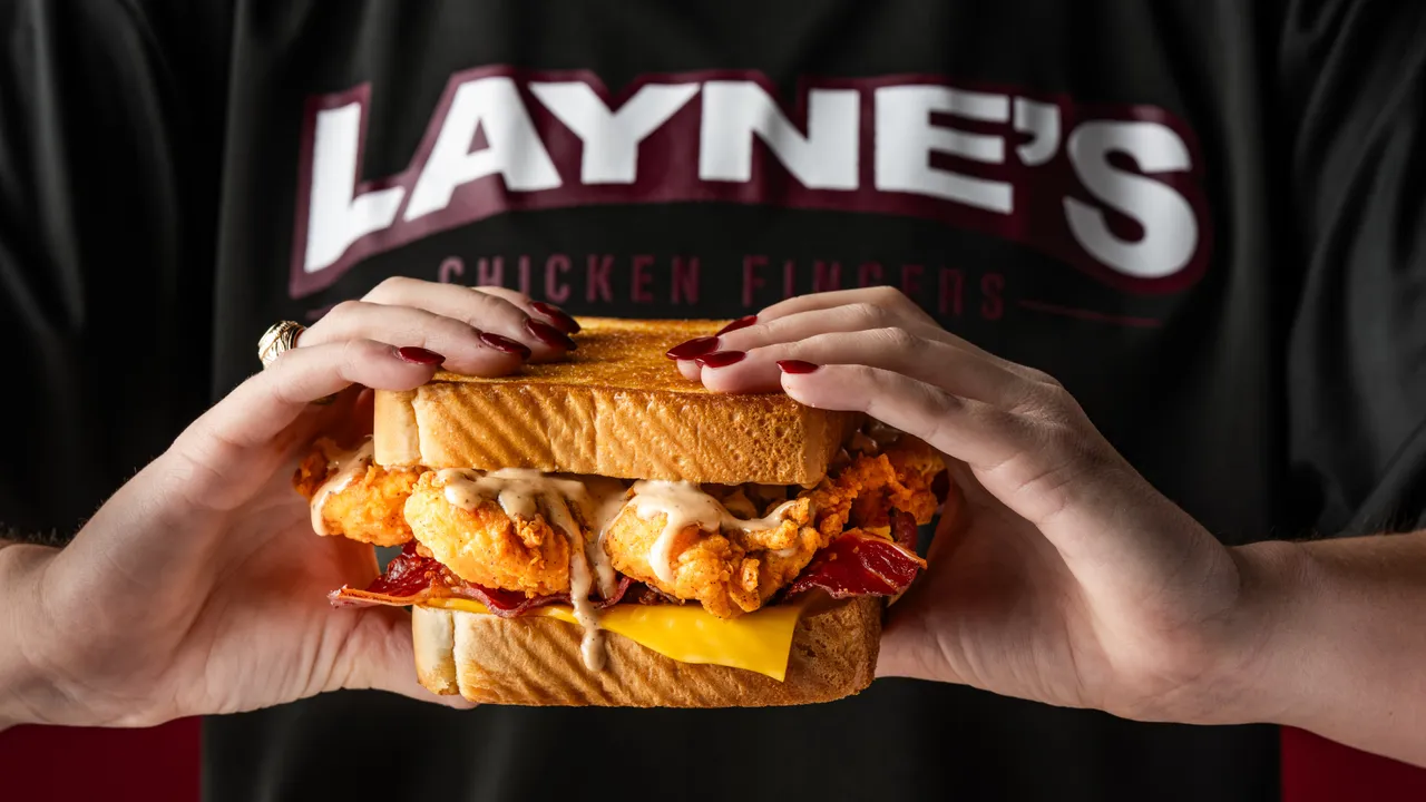 Close-up photo of person holding Layne's tender sandwich, wearing Layne's shirt
