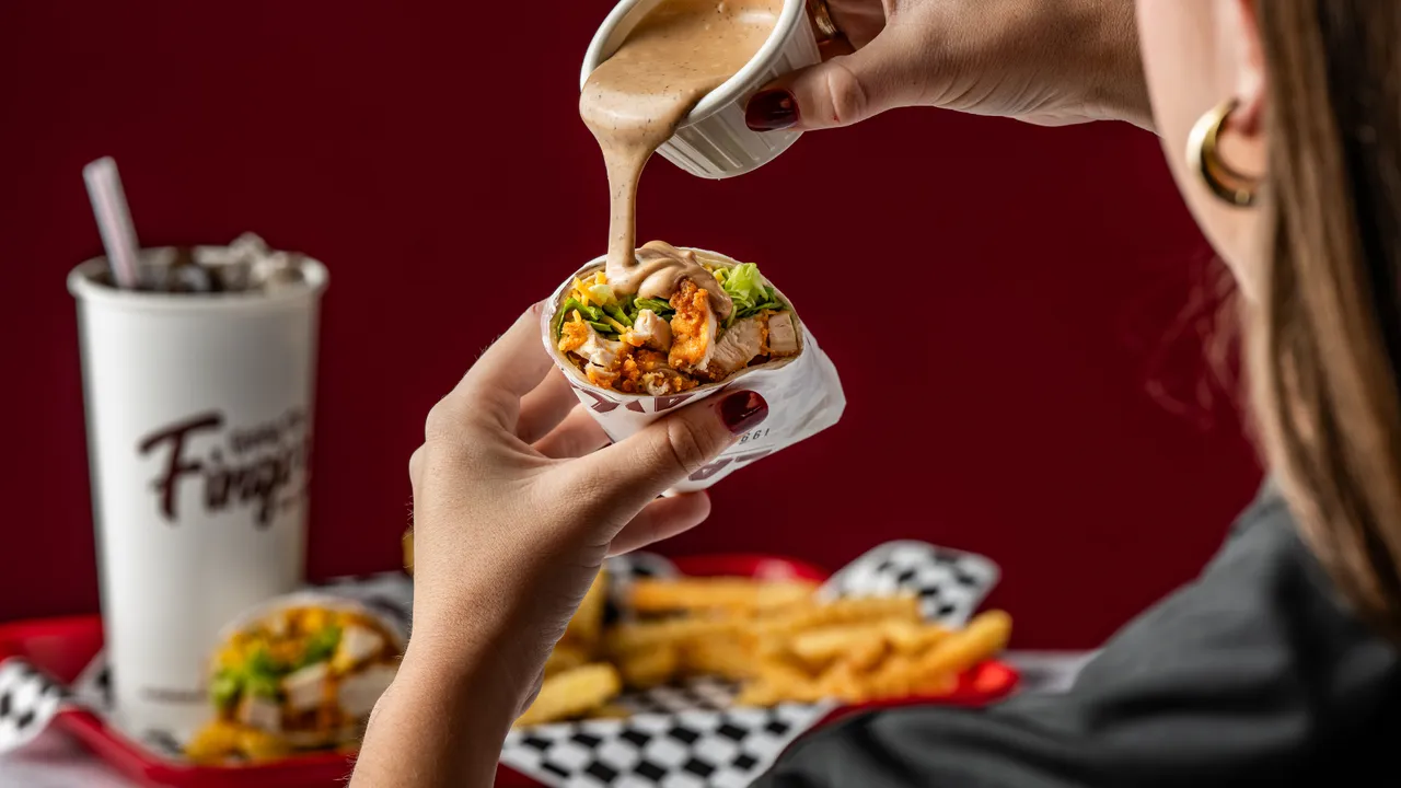 Photo of person holding Layne's Chicken Fingers wrap, pouring sauce