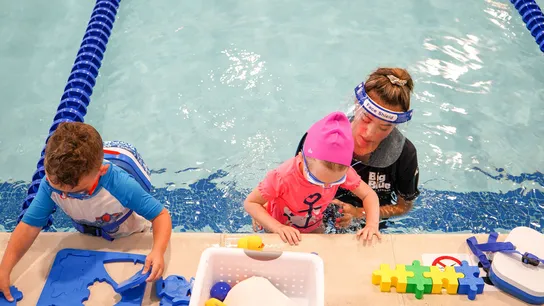 woman in pool wearing a face shield with two children