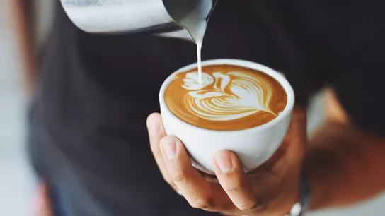 Man in coffee shop pouring decorative flower on cup of cappuccino.