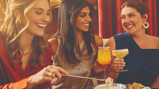 Melting Pot 50th anniversary photo, featuring three people enjoying celebratory drinks and fondue