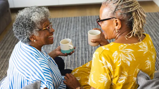 Photo of two people sitting together, holding mugs, smiling at each other