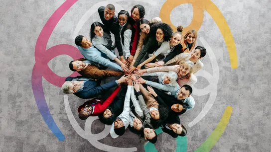 Photo of a large group of people standing in a circle, placing hands together in center