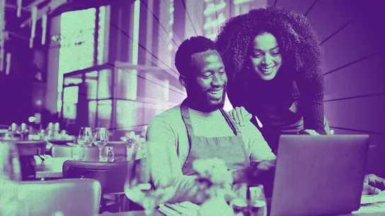 Photo of two people sitting in a restaurant, looking at a laptop