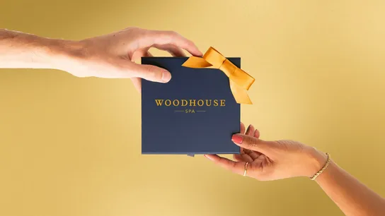 Photo of two hands holding Woodhouse Spa gift box against gold background
