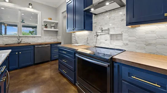 Photo of kitchen space with wooden counters, navy blue cabinets, and white and gray backsplash