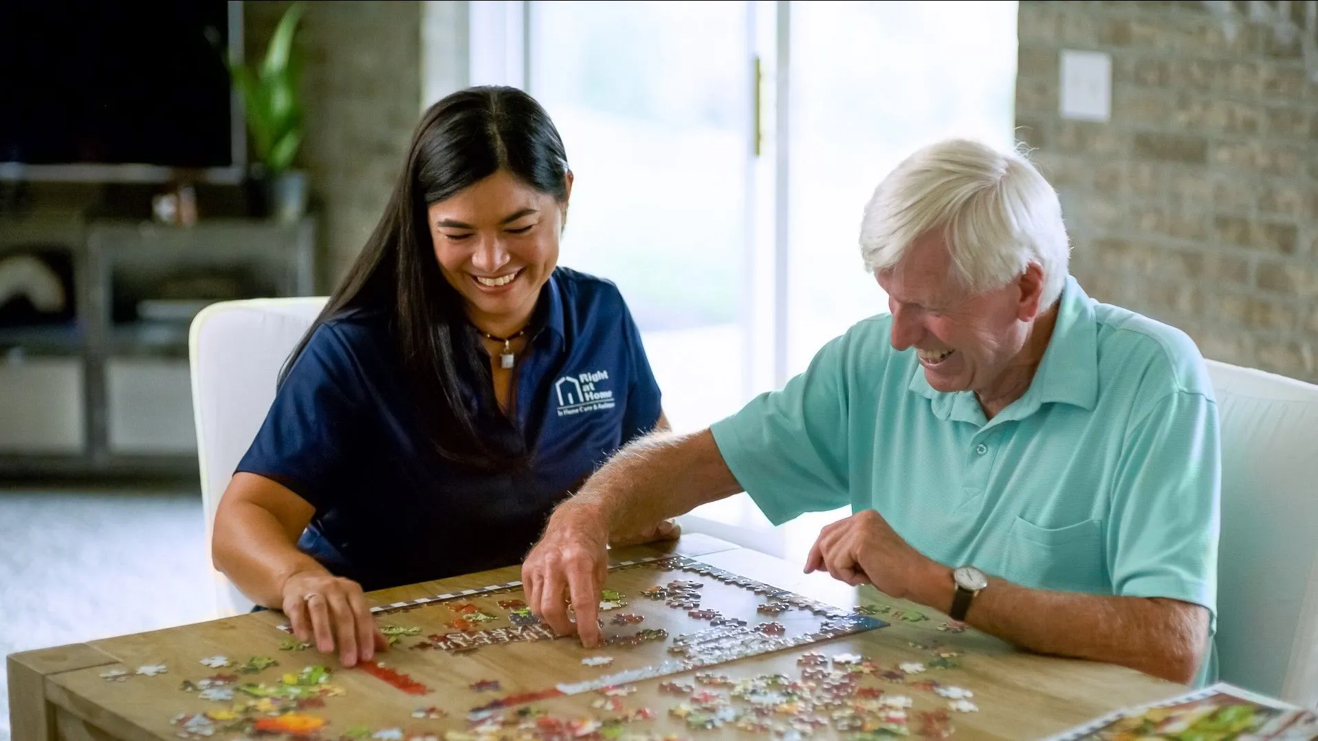 A woman Right at Home worker is completing a puzzle with an elderly man with white hair.