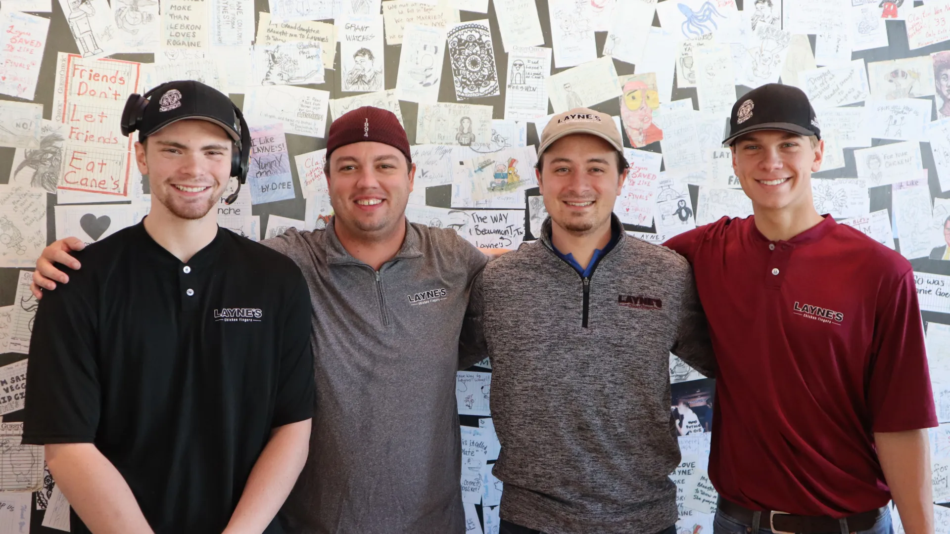 Four Layne's team members stand in front of a wall decorated with artwork from the community