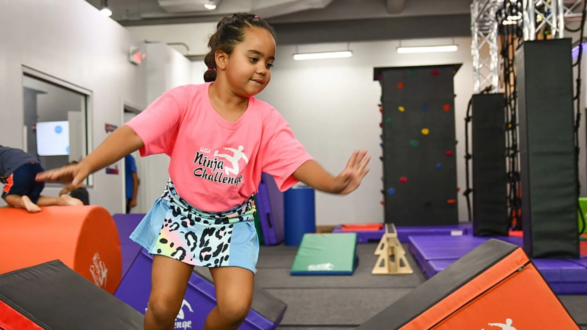 photo of child wearing pink USA Ninja Challenge shirt and athletic skirt navigating obstacle course