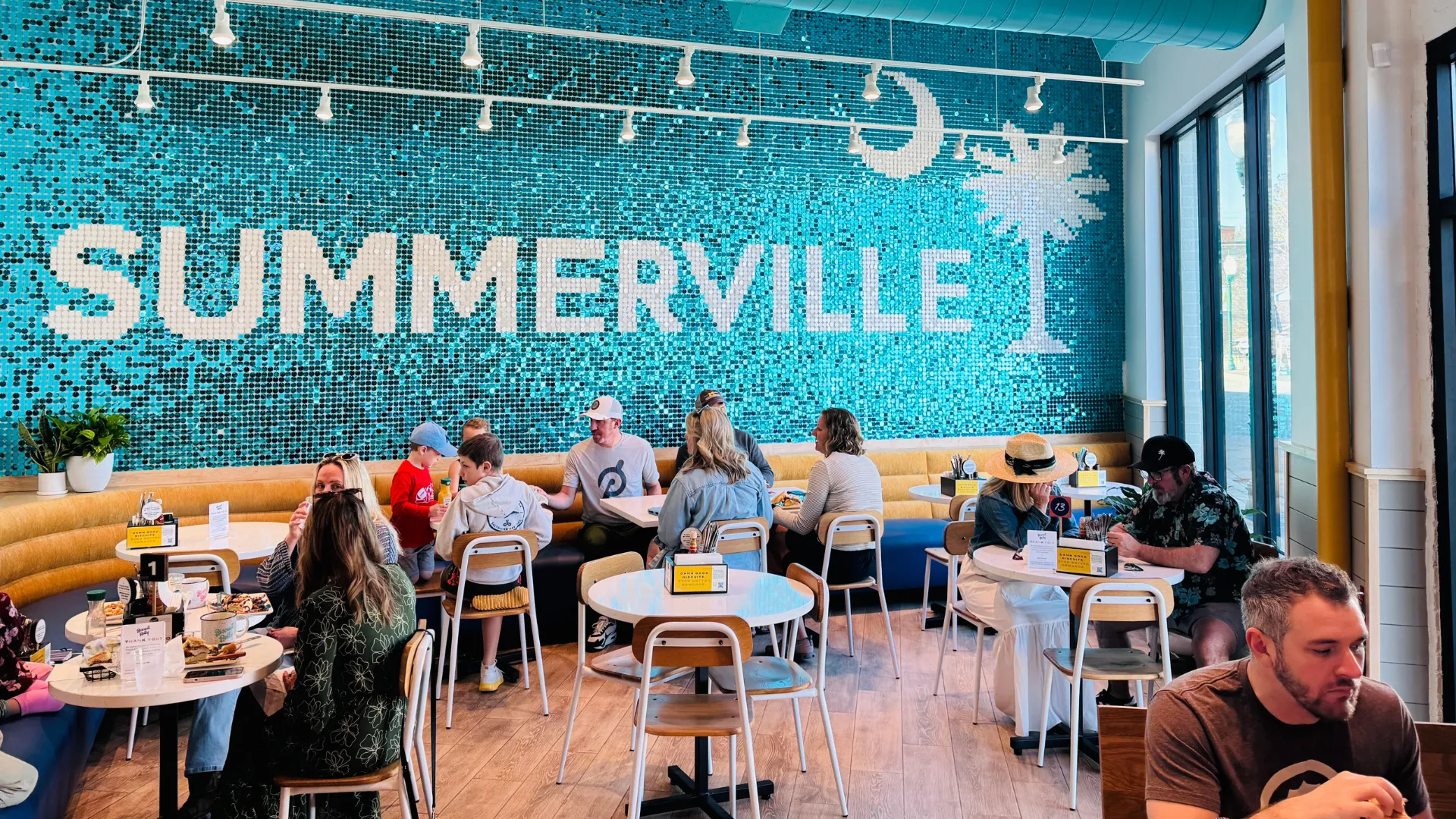 Photo of interior of Biscuit Belly Summerville featuring blue tile wall, tables with seated guests