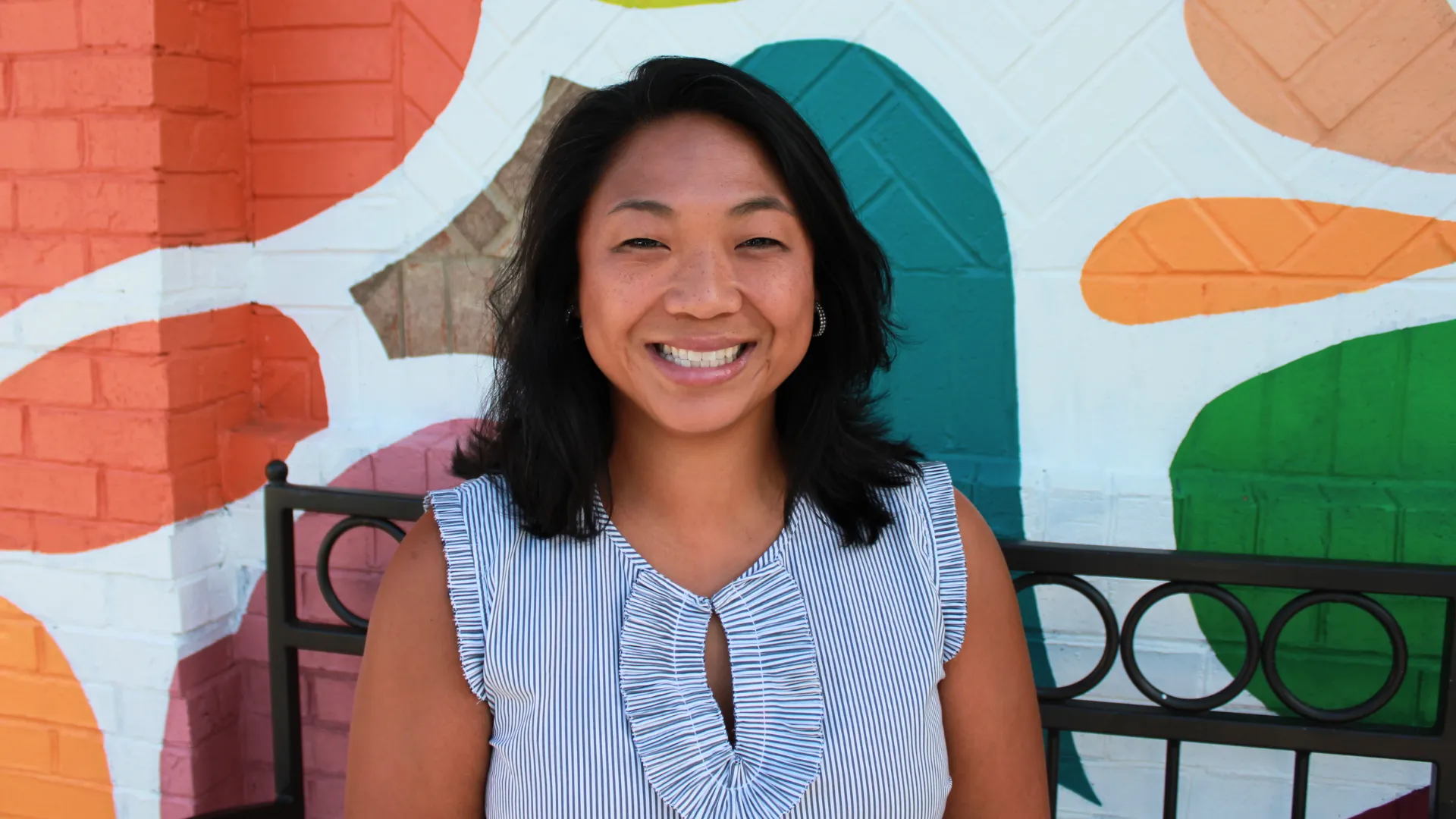 photo of Michelle Holliman, smiling, in front of a white brick wall with colorful mural