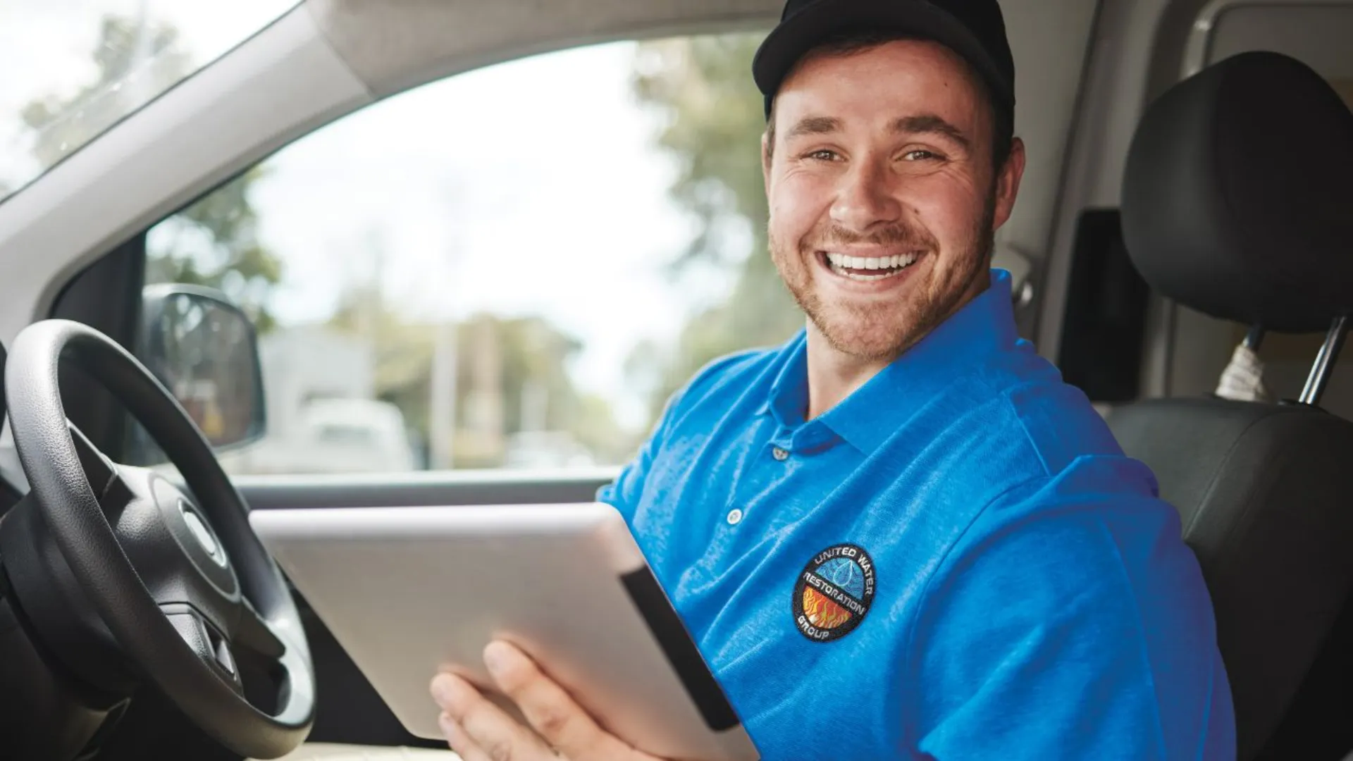 photo of a United Water Restoration Group team member in a car, smiling at the camera