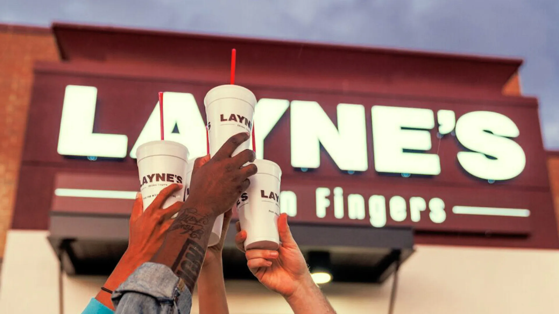 image of laynes chicken finger restaurant with 4 hands holding cups in the air to celebrate 