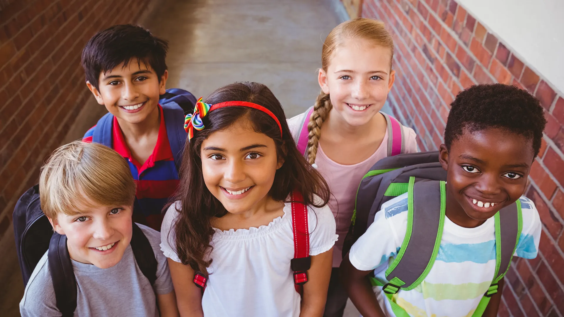 Photo of diverse group of school-aged children standing with backpacks, smiling at camera
